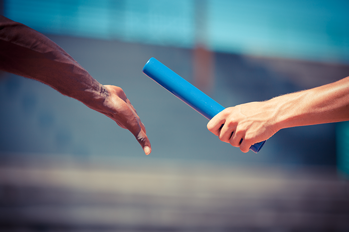 an image of one hand handing off the baton to another hand on a track field